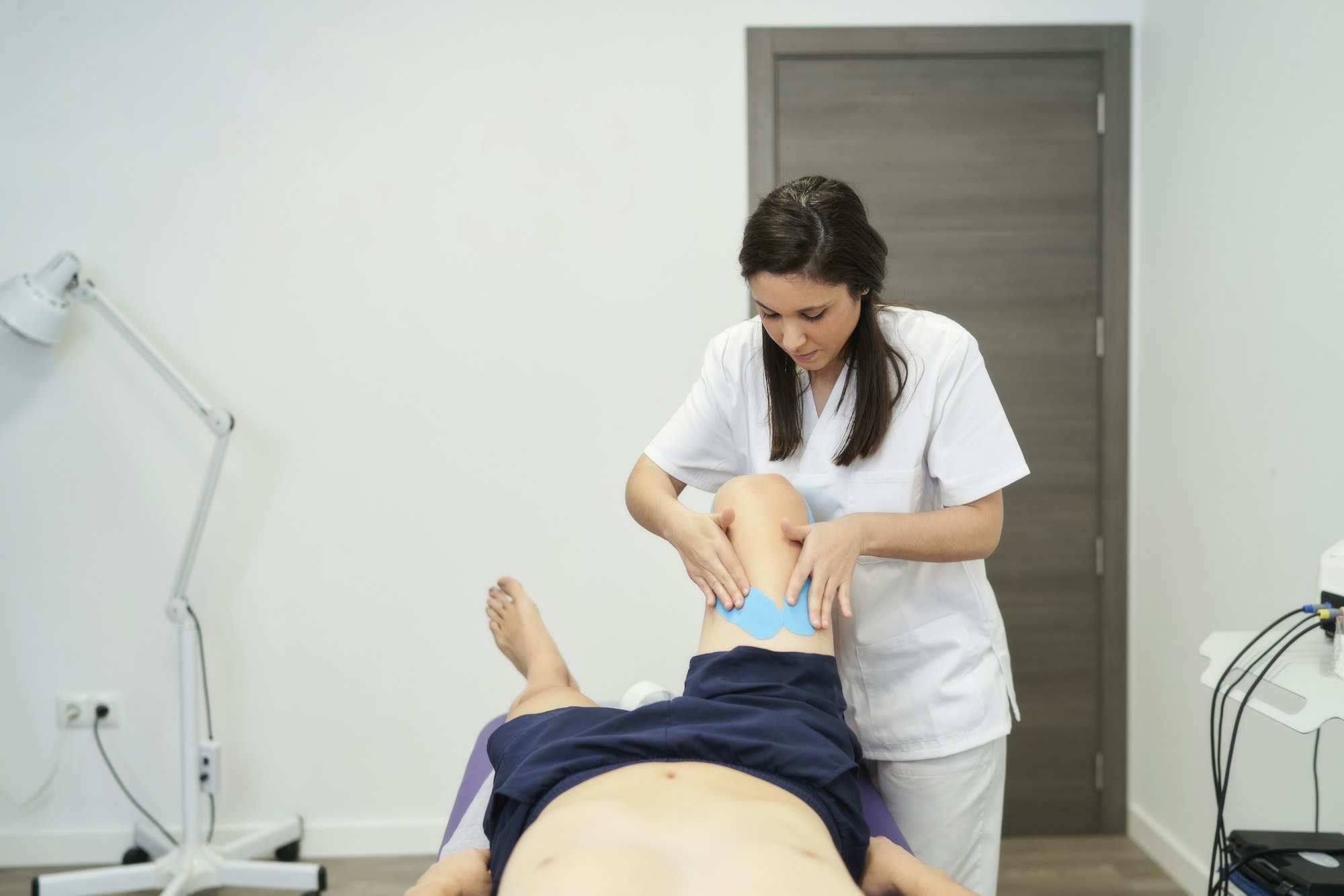 physiotherapist treating the patient's knee with neuromuscular taping