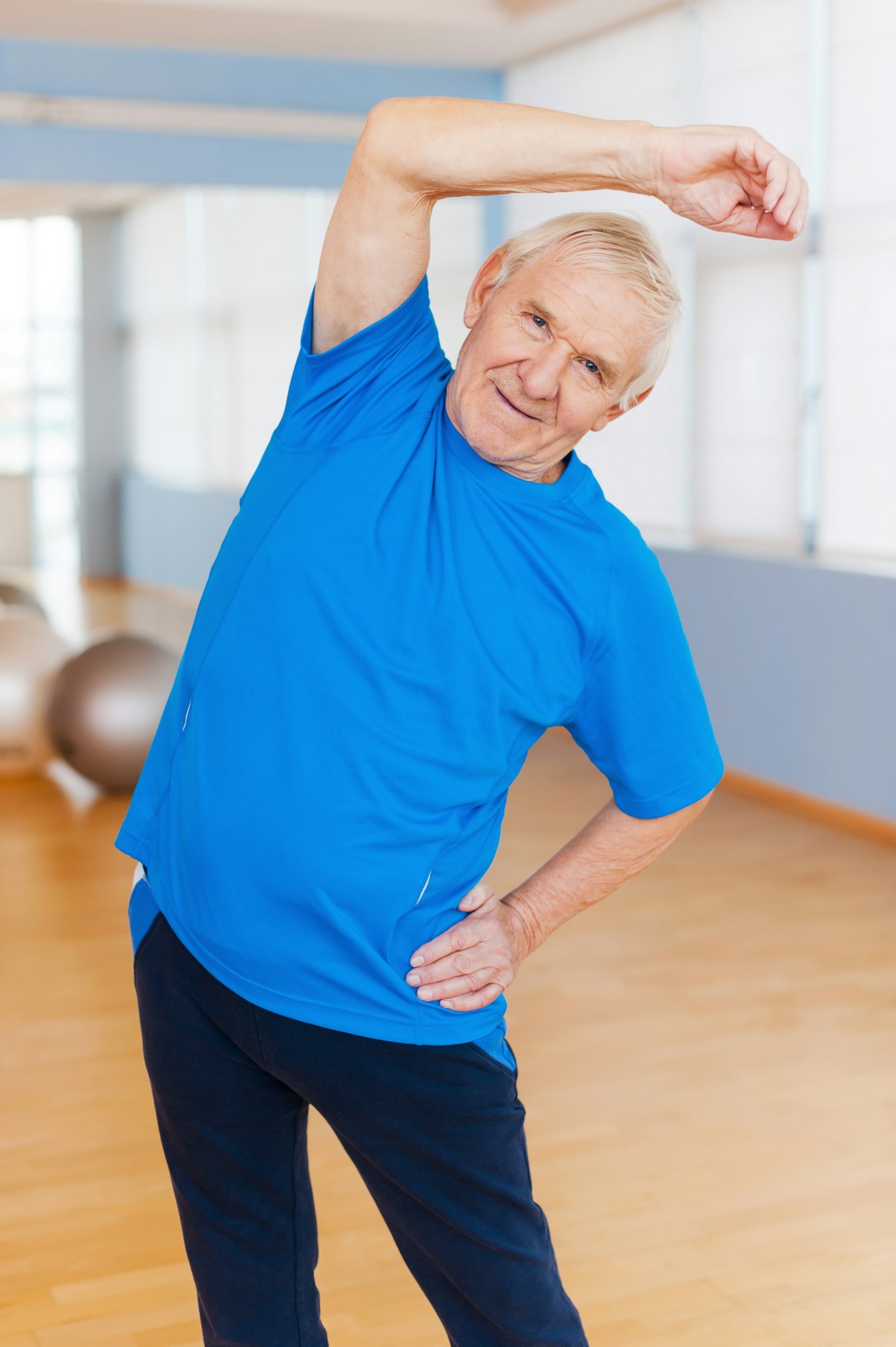 Staying active. Cheerful senior man doing stretching exercises and smiling while standing indoors